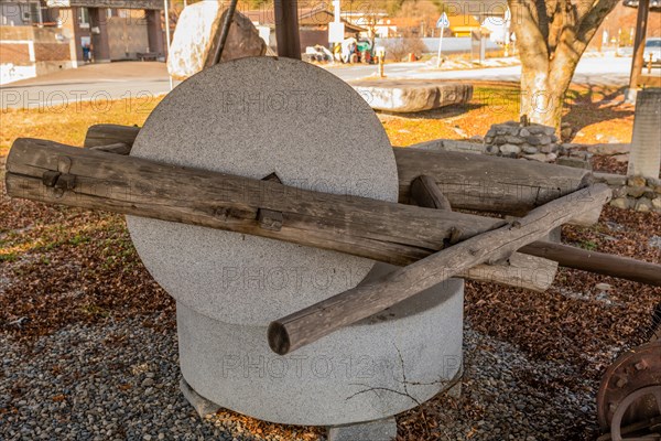 Old antique millstone and wheel in covered shelter with mountain community in background in South Korea