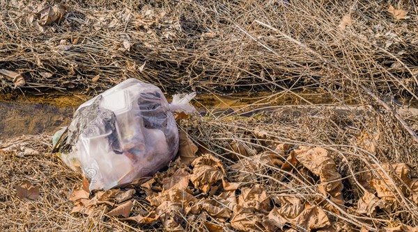 A crushed plastic bag amidst debris and dry grass highlights environmental pollution, in South Korea