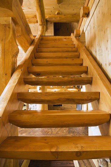 Wooden log stairs leading to upstairs floor inside handcrafted red cedar log cabin home, Quebec, Canada, North America