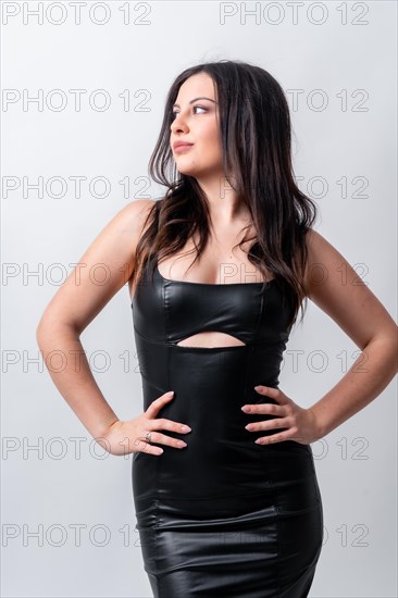 Studio photo with grey background of a model posing looking away wearing black long dress