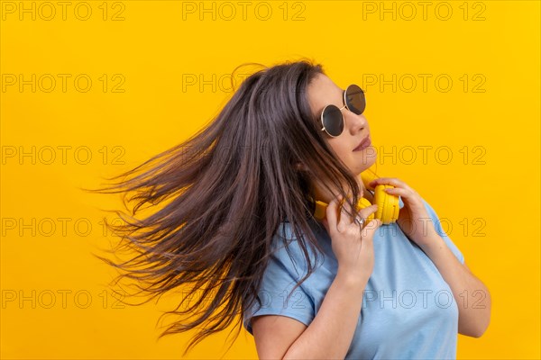 Studio portrait with yellow background of a woman waving the hair while using headphones