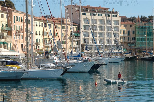 Sailing boats moored in a quiet harbour in front of colourful buildings under a clear blue sky Elba Island Italy