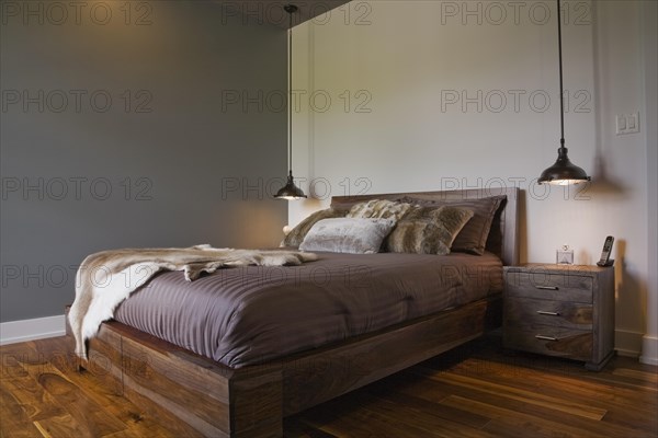 Queen size wooden base bed covered with fur pelt throw in guest bedroom inside luxurious home, Quebec, Canada, North America