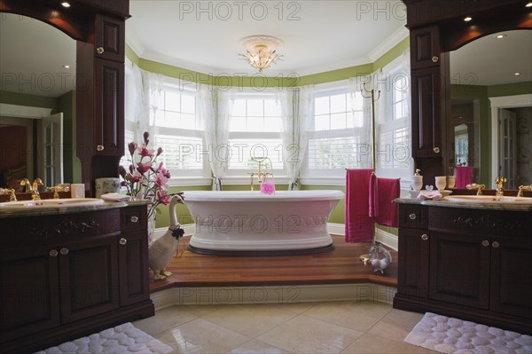 Master bedroom en suite with freestanding white bathtub on raised platform and his and her vanities inside elegant style home, Quebec, Canada, North America