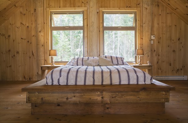 King size bed with wooden frame in master bedroom on upstairs floor inside handcrafted Eastern white pine Scandinavian log cabin home, Quebec, Canada, North America