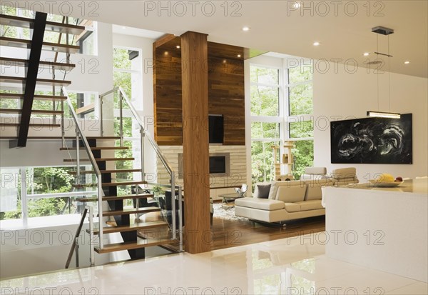 Wood, metal and glass staircase leading to living room with creamy beige L-shaped leather sofa inside luxurious home, Quebec, Canada, North America