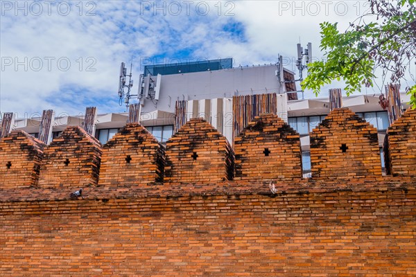 Ancient style brick wall with modern structures and cell towers behind, in Chiang Mai, Thailand, Asia