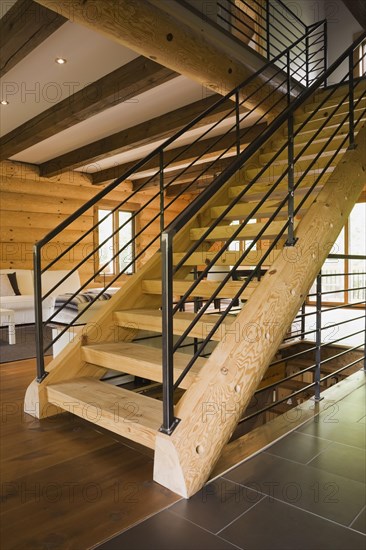 Wooden log stairs with black wrought iron railings and white cotton cloth upholstered sofas in living room inside contemporary style log home, Quebec, Canada, North America