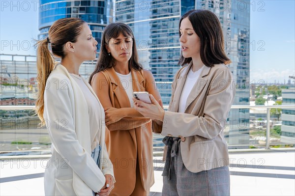 Three colleagues are on a terrace, one of them holding a cell phone and showing a business email to them