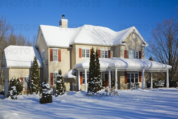 Two story beige vinyl siding with brownish red nuanced brick veneer and orange trim home in winter, Quebec, Canada, North America
