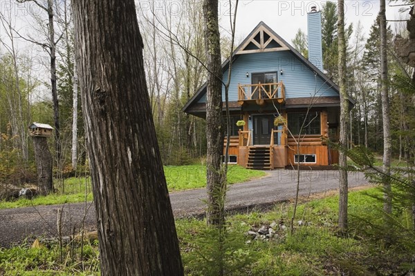 Post and beam cottage style hybrid log home facade with blue clapboard trim and timber elements in spring, Quebec, Canada, North America