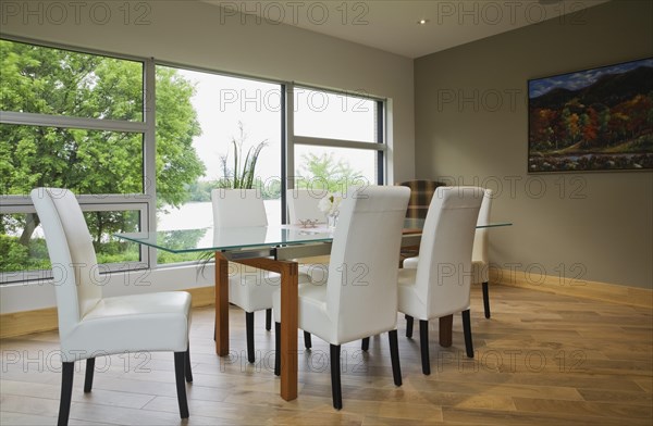 Clear glass top table with white leather high back chairs in dining room with beige ceramic tile floor inside modern cubist style home, Quebec, Canada, North America