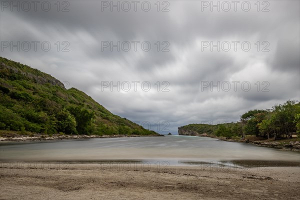 Rocky coast, long bay by the sea at sunset. Dangerous view of the Caribbean Sea. Tropical climate on a cloudy day in La Porte d'Enfer, Grande Terre, Guadeloupe, French Antilles, North America