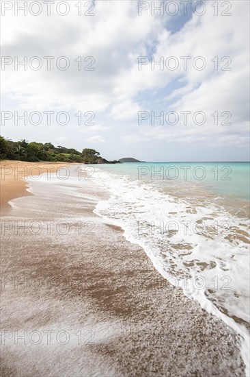 Lonely, wide sandy beach with turquoise-coloured sea. Tropical plants in a bay in the Caribbean sunshine. Plage de Cluny, Basse Terre, Guadeloupe, French Antilles, North America