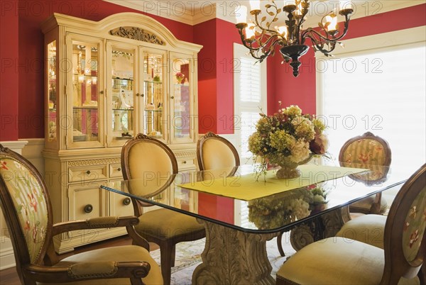 Glass top table with high-back wooden and upholstered chairs in dining room with buffet inside elegant style home, Quebec, Canada, North America