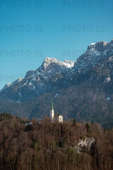 St. Niklaus Church in front of the snow-covered Zahmer Kaiser, surrounded by forest under a clear blue sky, Ebbs, Tyrol, Austria, Europe