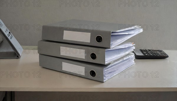 Stacks of documents in grey file folders on a desk next to a calculator, symbolism bureaucracy, AI generated, AI generated