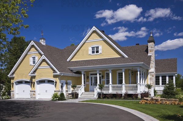 Yellow and white trim contemporary country house with two car garage, landscaped front yard and black asphalt driveway in summer, Quebec, Canada, North America