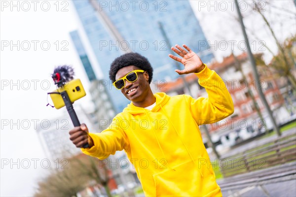 Cool african young content creator waving at camera steaming live standing in a city