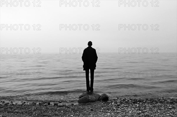 Young man stands on the beach in cloudy weather and looks at the Baltic Sea, Gross Schwansee, Mecklenburg-Vorpommern, Germany, Europe