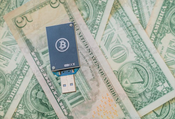 A dark blue USB hardware wallet with a Bitcoin logo on a background of US dollar bills, in South Korea