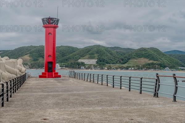 A vibrant red lighthouse stands on the pier with ocean and hills in the background, in Ulsan, South Korea, Asia