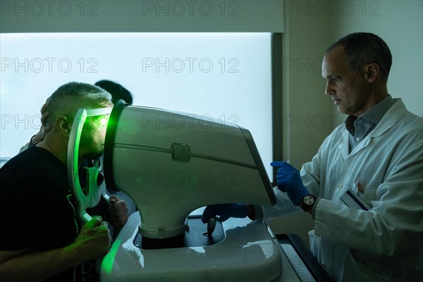 Dark photo of a clinic with ophthalmologist treating glaucoma on a senior man using laser machine