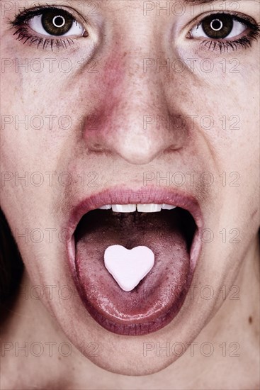 Woman with a heart of glucose on her outstretched tongue, studio shot, Germany, Europe