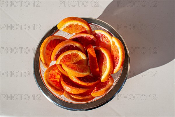 A glass bowl full of fresh orange slices in the sunlight, from above