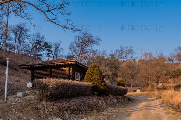 Log cabin next to dirt road in mountain park on winter day under clear blue sky in Boeun, South Korea, Asia