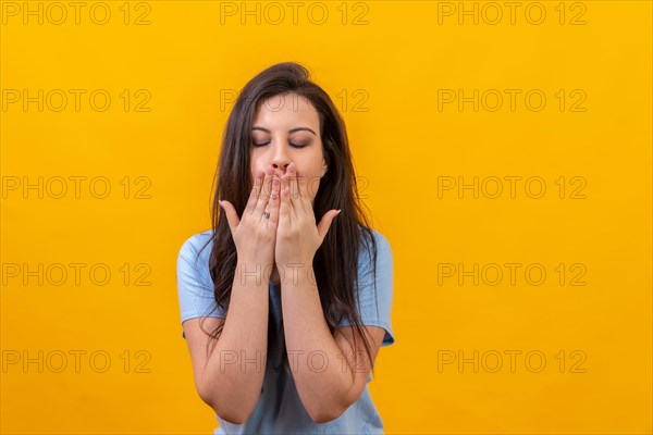 Studio portrait with yellow background of a casual woman blowing a kiss closing eyes