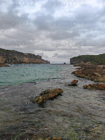 Rocky coast, long bay by the sea at sunset. Dangerous view of the Caribbean Sea. Tropical climate on a cloudy day in La Porte d'Enfer, Grande Terre, Guadeloupe, French Antilles, North America