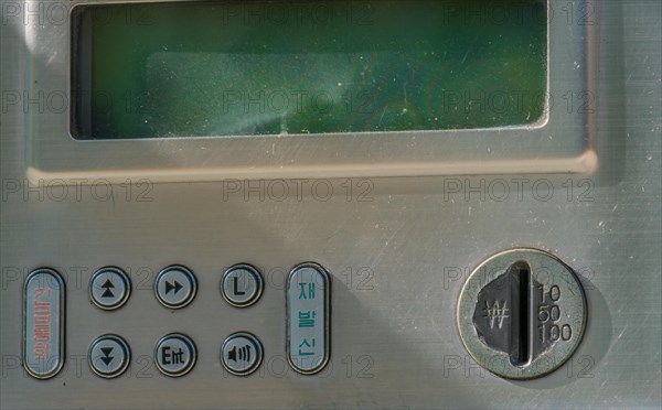 A close-up of a weathered control panel with digital display and coin slot, in South Korea
