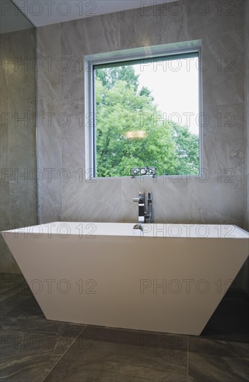 White freestanding vessel shaped bathtub in bathroom with grey ceramic tile floor and walls on ground floor inside modern cubist style home, Quebec, Canada, North America