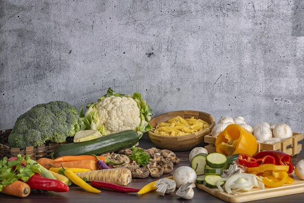 Various fresh vegetables such as peppers, cauliflower, peppers, mushrooms, broccoli and pasta next to and on a wooden board on a wooden surface