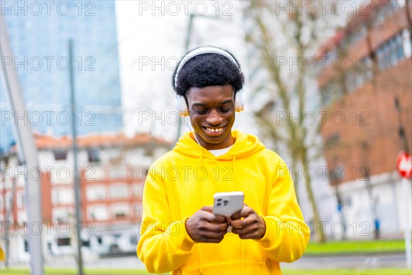 Cool and happy african young man listening to music using mobile in the city