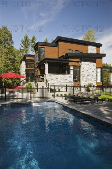 Two story grey, beige and tan cut stone with wood siding and black trim home and inground swimming pool in summer, Quebec, Canada, North America