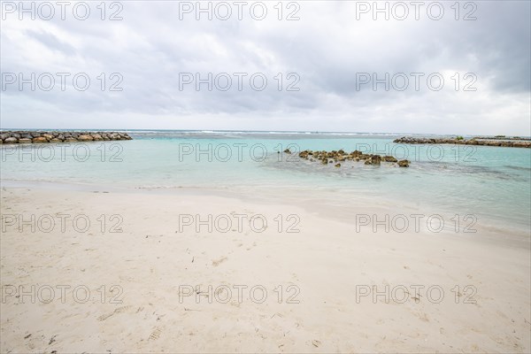 Caribbean dream beach with palm trees, white sandy beach and turquoise-coloured, crystal-clear water in the sea. Shallow bay on a cloudy day. Plage de Sainte Anne, Grande Terre, Guadeloupe, French Antilles, North America