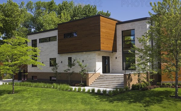 Beige stone with brown stained cedar wood modern cubist style residential home facade in spring, Quebec, Canada, North America