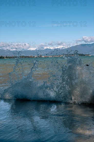 Water splashes in the foreground with the town of Sirmione and blue sky in the background, Sirmione, Lake Garda, Italy, Europe