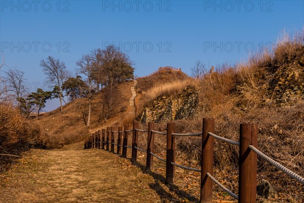 Rope fence next to hiking trail to wooden stairway up side of mountain under blue sky in Boeun, South Korea, Asia