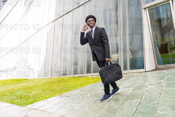 Full length portrait of a cool african businessman talking to the mobile walking in the city