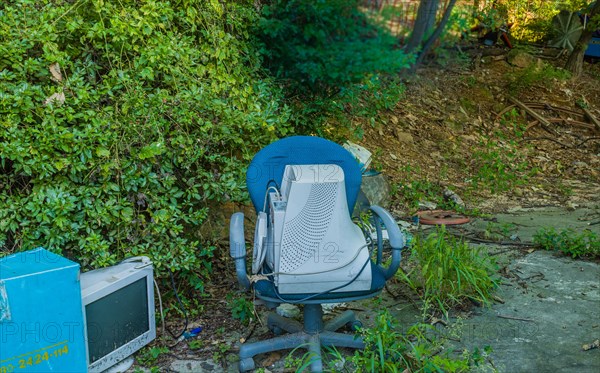 Old CRT computer monitors discarded in rural wooded area. One in old chair the other on the ground next to blue container in Seoul, South Korea, Asia