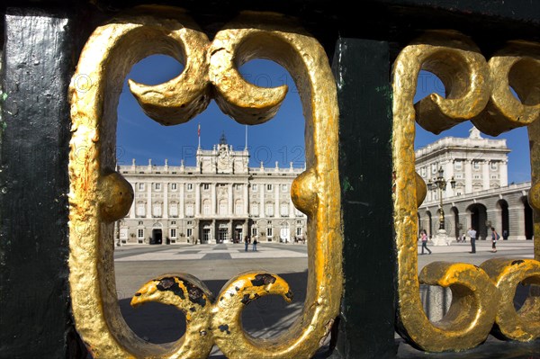 View of a historic royal palace through a gold-decorated wrought-iron gate, blue sky with clouds in the background Madrid Spain