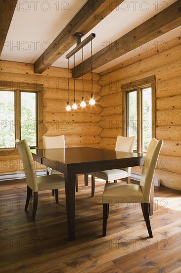 Brown wooden table and white cotton cloth upholstered high back chairs in dining room inside contemporary style log home, Quebec, Canada, North America