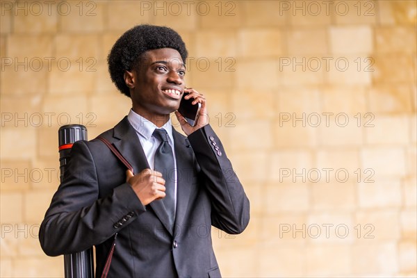 Horizontal photo with copy space of an young african american architect wearing suit talking to the mobile phone in the city next to a urban wall