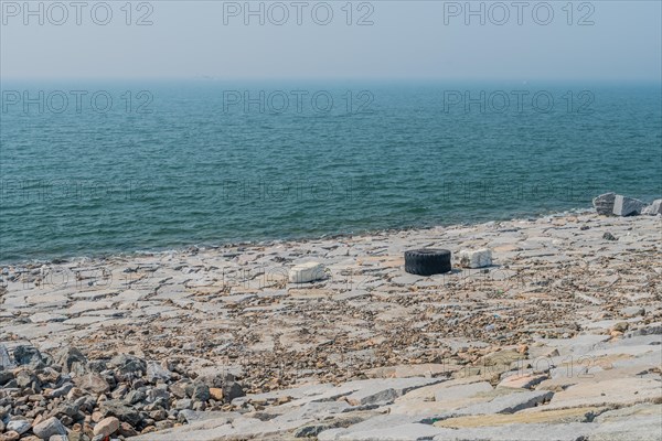 Wide view of a rocky coast polluted with waste and a tire, in South Korea