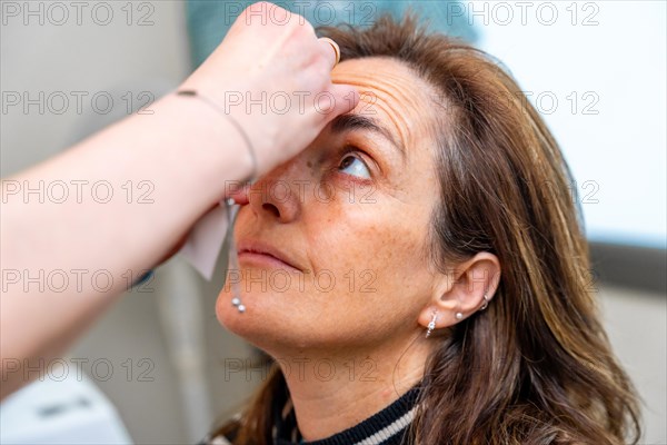 Ophthalmologist applies drops to dilate the pupil to a mature woman before a glaucoma test on the eye with a laser machine