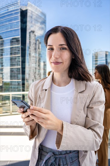 A woman dressed in business attire is standing outside with a cell phone in her hand and about to use it