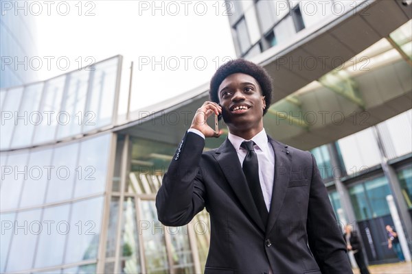 Low angle view portrait of a young busy african businessman talking to the mobile while commuting in the city